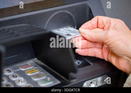 Vista ravvicinata di una donna anziana che inserisce una carta di credito nel modo sbagliato nello slot bancomat nero, illustrando la difficoltà e la confusione Foto Stock