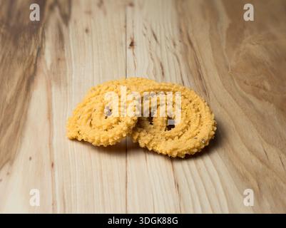 Un paio di croccanti stuzzichini murukku indiani speziati disposti su una superficie di legno naturale. Fotografia di cibo caldo e rustico con spazio per copie commerciali. Foto Stock