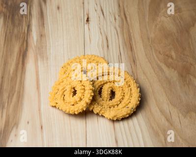 Primo piano di tre stuzzichini di murukku croccanti e piccanti impilati su uno sfondo a grana di legno chiaro. Ideale per il food blogging e il marketing della cucina etnica. Foto Stock