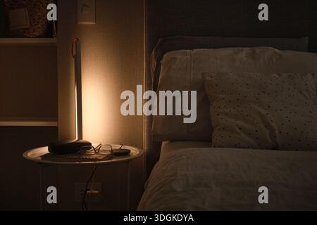 Lampada moderna che illumina un comodino e un letto in una camera buia di notte Foto Stock