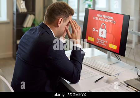 Uomo d'affari stressato che affronta ransomware su un computer dell'ufficio con file crittografati Foto Stock