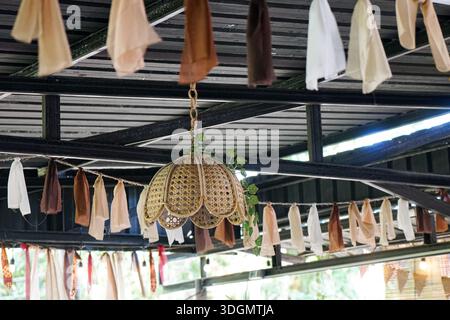 Lampada in rattan intrecciato con bordi smerlati appesi in uno spazio esterno accogliente e decorato con viti. Foto Stock