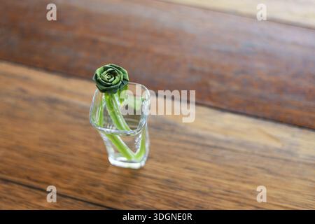 Foglia di panda verde fresco piegata in forma di fiore di rosa artificiale all'interno di una piccola superficie in legno di vetro trasparente che mostra la creazione naturale di erbe biologiche Foto Stock