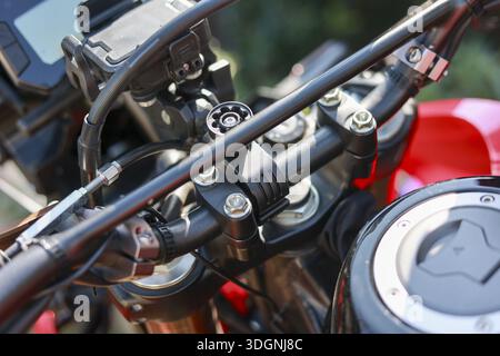 Foto ravvicinata che mostra i dettagli del manubrio rosso della motocicletta, del tappo del serbatoio del carburante e del robusto supporto in metallo che evocano una sensazione di libertà e un viaggio avventuroso Foto Stock