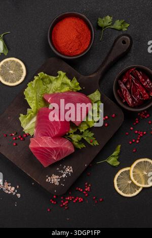 Bistecche di tonno sashimi crude su lattuga croccante con fette di limone, paprika, peperoncini secchi, sale rosa dell'himalaya e grani rossi ingredienti vivaci Foto Stock