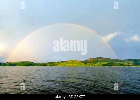 Un vivace arcobaleno si affaccia sul lago Mutanda a Kisoro, nel sud-ovest dell'Uganda, mentre la luce del sole si irrompe attraverso le nuvole di pioggia e si riflette sull'altopiano calmo Foto Stock