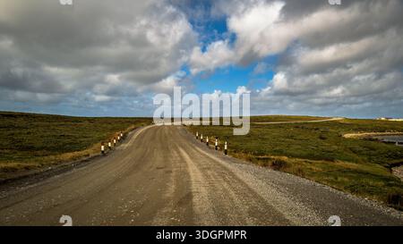Una remota strada delle Isole Falkland si snoda attraverso colline ondulate che conducono verso un orizzonte lontano sotto un cielo dinamico con nuvole e macchie sparse Foto Stock