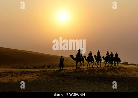 Silhouette di Tuareg che guida un treno a cammello sotto il sole del tramonto, Erg Chebbi, Merzouga, deserto del Sahara, Marocco Foto Stock