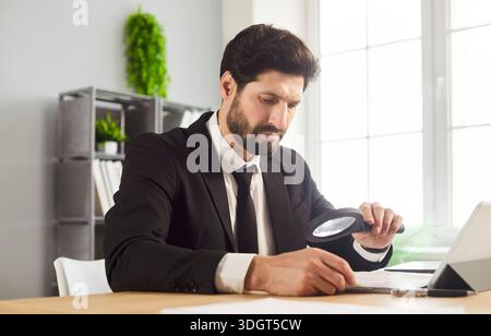 Primo piano di un uomo d'affari che controlla i documenti e rivede i dati con una lente di ingrandimento Foto Stock