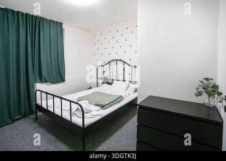 camera da letto con interni luminosi, mobili neri e tende verdi Foto Stock