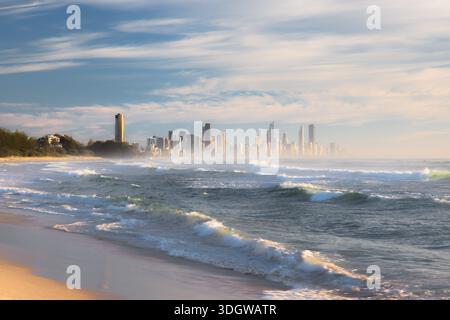 Luci e onde del mattino d'oro che arrivano a riva a Burleigh Heads Beach, Gold Coast, Queensland con lo skyline cittadino di Surfers Paradise. Foto Stock