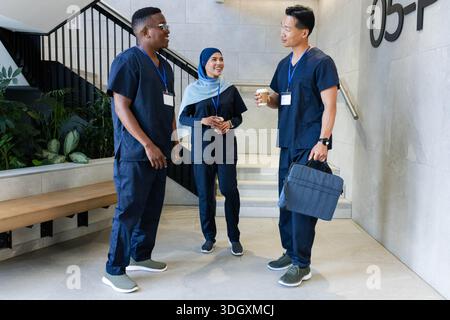 Diversi operatori sanitari in scrub della marina in piedi e chiacchierare nella hall della clinica, tenendo una tazza di caffè Foto Stock