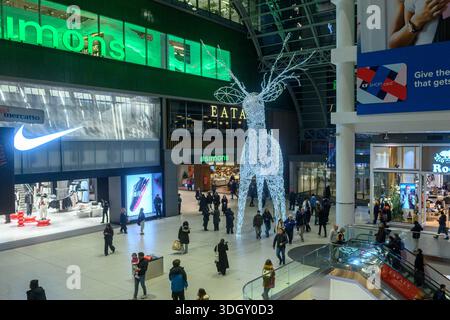 Toronto, ON, Canada - 24 dicembre 2025: Gli amanti dello shopping camminano attraverso un affollato centro commerciale a più piani caratterizzato da una grande e luminosa decorazione con renne Foto Stock
