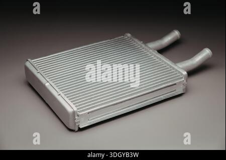Immagine ravvicinata di uno scambiatore di calore in metallo argento con due tubi sporgenti su uno sfondo scuro. Lo scambiatore di calore è dotato di una struttura simile a una griglia wi Foto Stock