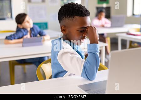 Diversi bambini in classe in classe, ragazzo afroamericano con tetto blu che usa un computer portatile o un tablet nelle vicinanze Foto Stock