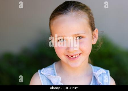 Bambina sorridente che indossa un top senza maniche azzurro con finiture in pizzo e cravatta in giardino Foto Stock