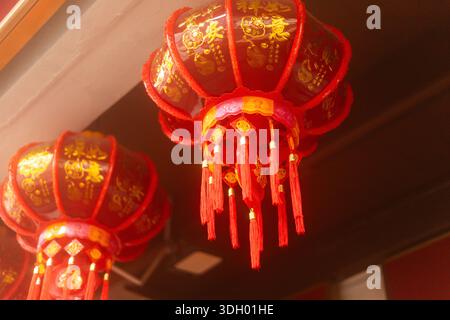Lanterne rosse con disegni in oro sono sospese dal soffitto in un'area decorata. Queste lanterne fanno parte di una celebrazione con elementi tradizionali. Foto Stock