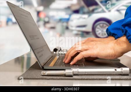 Primo piano delle mani del manager presso l'officina di riparazione auto che pianifica le operazioni utilizzando un computer portatile Foto Stock