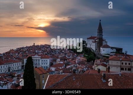 Tramonto sulla città vecchia con tetti di tegole rosse, con la chiesa parrocchiale di San Giorgio e il suo campanile che si affaccia sul mare Adriatico. Foto Stock