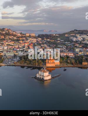 Veduta aerea dell'incantevole Casina Vanvitelliana che si specchia nel tranquillo lago di Fusaro, bordato dai vivaci edifici della città, Bacoli, Campania, Ital Foto Stock