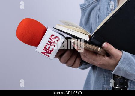 Primo piano di un giornalista che tiene in mano un microfono e un taccuino durante l'intervista Foto Stock