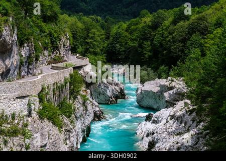 Una tortuosa strada in pietra lungo una scogliera rocciosa che si affaccia sul turchese fiume Soca, con una fitta foresta verde in lontananza. Foto Stock