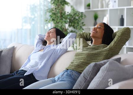Due diverse donne si rilassano e riposano sedute su un divano a casa Foto Stock