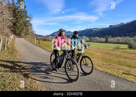 Una coppia di anziani fa un giro in mountain bike elettrica su un sentiero nelle Alpi di Allgäu vicino a Oberstaufen in Baviera. La scena raffigura un paesaggio montano ventoso Foto Stock