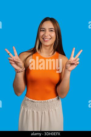 Giovane donna sorridente allegramente e che fa segni di pace con entrambe le mani Foto Stock