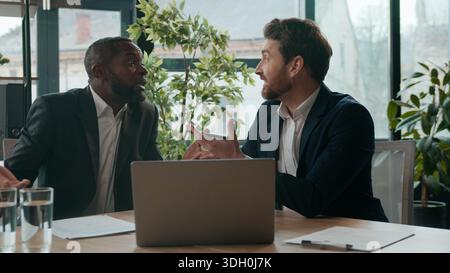 Uomini eterogenei colleghi team aziendali che condividono idee lavoro portatile discussione durante una riunione d'ufficio sorridente due uomini d'affari multirazziali entusiasti Foto Stock