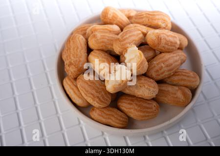 primo piano sopra la testa di una ciotola di ceramica ricoperta di mini choux di colore dorato, una fetta per rivelare una cremosa ripiena di vaniglia, su una tonda bianca piastrellata Foto Stock