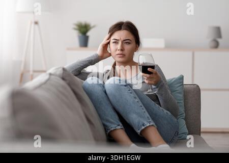 Triste frustrato giovane donna caucasica con un bicchiere di vino che soffre di depressione, stress e lavoro eccessivo a casa Foto Stock