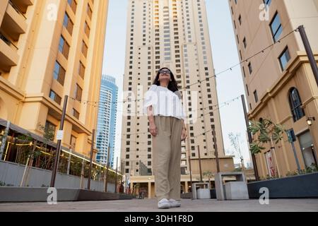 La moderna città di Dubai vive con una donna in piedi tra grattacieli contemporanei, vista ad angolo basso Foto Stock