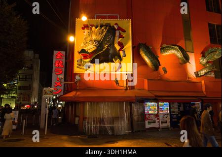 Osaka, Giappone - 5 novembre 2023: Grande scultura del drago e segnaletica rossa illuminata di ramen all'esterno del ristorante Kinryu Ramen nel quartiere Dotonbori di notte, con distributori automatici e pedoni visibili sulla strada. Foto Stock