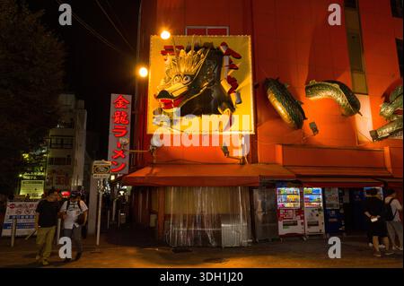 Osaka, Giappone - 5 novembre 2023: Esterno del ristorante Kinryu Ramen a Dotonbori di notte, caratterizzato da un grande cartello con la testa di drago illuminato, elementi scultorei di drago sul muro, segnaletica rossa con scritta giapponese e diversi distributori automatici lungo il marciapiede con persone nelle vicinanze. Foto Stock