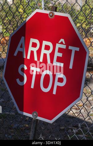 Primo piano di arret francese bilingue rosso brillante e segnale di stop inglese con recinzione in rete metallica sullo sfondo, Quebec, Canada Foto Stock