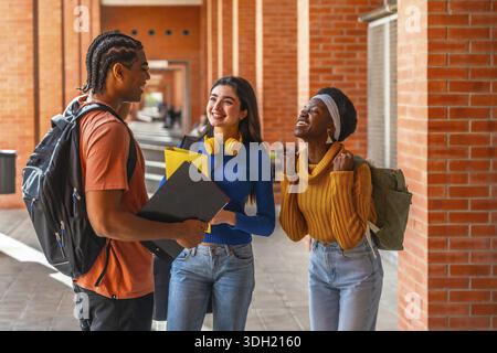 Gruppo di giovani studenti universitari felici di diverse etnie che comunicano e celebrano il successo su un passaggio pedonale del campus universitario, godendo di un'istruzione Foto Stock