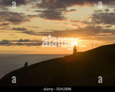 Vista aerea del sole che tramonta dietro la sagoma di San Juan de Gaztelugatxe, che proietta un bagliore dorato sul mare, Gaztelugatxeko Doniene, Basco C. Foto Stock
