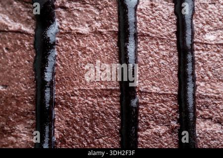 Primo piano di lucenti ganache al cioccolato fondente che gocciolano verticalmente su una torta con crema di burro di cacao, creando un delizioso motivo lineare. Foto Stock