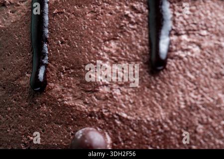 Primo piano di lucenti ganache al cioccolato fondente che gocciolano verticalmente su una torta con crema di burro di cacao, creando un delizioso motivo lineare. Foto Stock