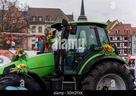 Trattore decorato composizioni floreali colorate durante la sfilata di Carnevale di Fasching nel centro di Erfurt. Macchinari agricoli festivi architettura storica Foto Stock