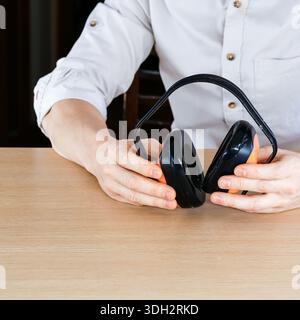 Mani che afferrano cuffie a cancellazione del rumore nere e arancioni su una superficie in legno per scatti ravvicinati Foto Stock