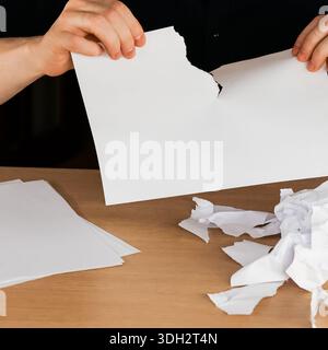 Persona che strappa la carta bianca con frustrazione sopra il tavolo disseminata di pezzi rotti e strappati Foto Stock