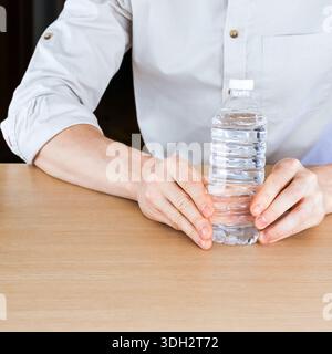 Primo piano di mani maschili tenendo delicatamente una bottiglia di plastica trasparente riempita d'acqua Foto Stock