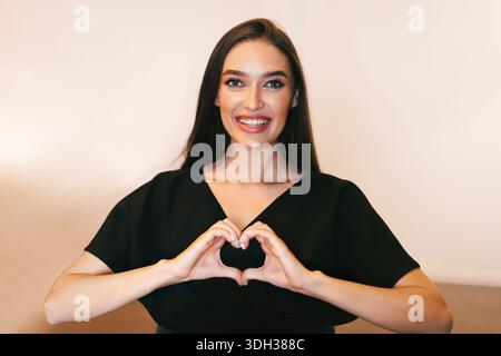 Donna sorridente felice facendo il cuore forma con le mani Foto Stock