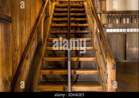 Himeji, Giappone - 31 ottobre 2023: Una ripida scala in legno con corrimano è visibile all'interno del donjon del castello di Himeji, circondato da pareti e pavimenti in legno. Foto Stock