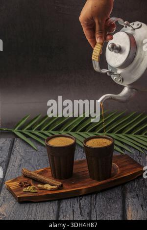 Una persona sta versando il tè masala nella tazza Bio chai. Le tazze sono su un tavolo di legno. Tagliare il chai che viene versato dal bollitore del tè. Foto Stock