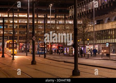 Manchester, Inghilterra, 3 marzo 2024: Scena serale di strada ai Piccadilly Gardens con tram, autobus, pedoni ed edifici moderni illuminati. Foto Stock
