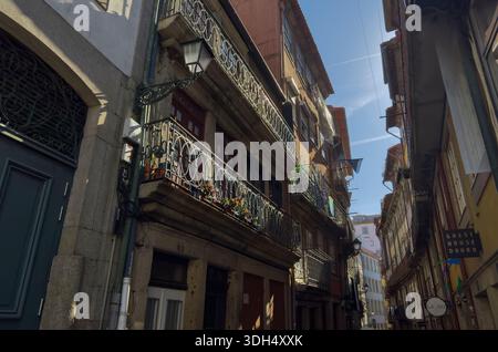 Porto, Portogallo, 20 maggio 2025, stretta strada vecchia con case tradizionali con balconi in ferro battuto e persiane in legno. Calda luce solare pomeridiana Foto Stock