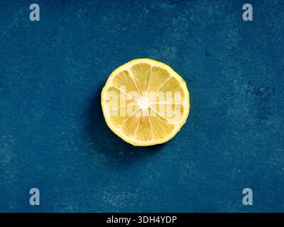 Fetta di limone giallo brillante isolata su uno sfondo blu scuro. Concetto di agrumi freschi Foto Stock